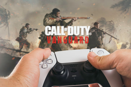 Male hand holding a Playstation 5 Dual Sense Controller with Call of Duty Vanguard game blurred in...