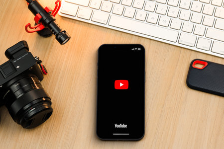 Youtube app on smartphone iPhone 13 Pro screen on wooden table. Content creator environment with keyboard, camera and mic. Rio de Janeiro, RJ, Brazil. October 2021.のeditorial素材