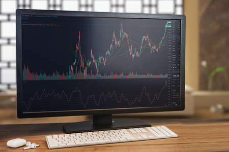 Financial stock market graph on computer screen. Monitor, keyboard and airpods on wooden table....