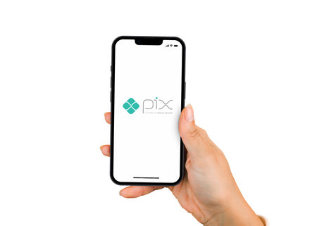 Female hand holding a smartphone iPhone 13 Pro with Pix app on the screen. White background. Rio de Janeiro, RJ, Brazil. November 2021.のeditorial素材