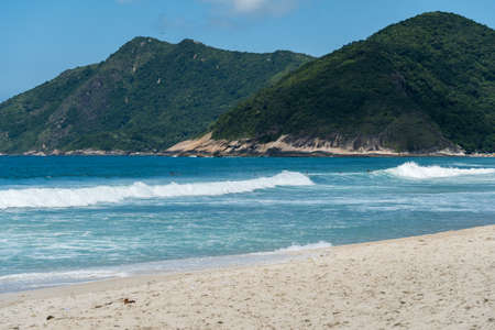 Grumari beach near Barra da Tijuca in Rio de Janeiro, Brazil. Sunny day with blue sky, clear water and small waves. Hills and nature around.の写真素材