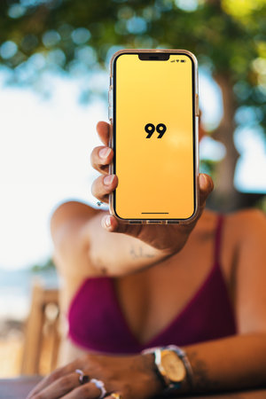 Girl on the beach holding a smartphone with 99 app on the screen. Rio de Janeiro, RJ, Brazil. March 2022.のeditorial素材