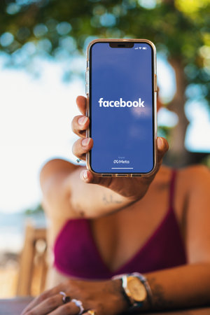 Girl on the beach holding a smartphone with Facebook app on the screen. Rio de Janeiro, RJ, Brazil. March 2022.のeditorial素材