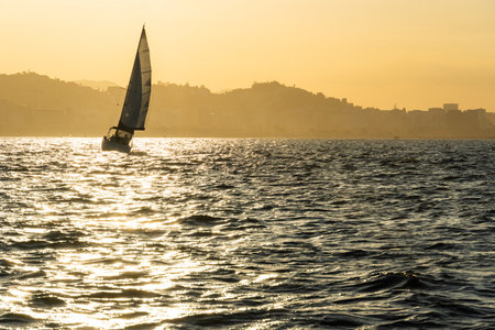 Sailing boat in Guanabara Bay in Rio de Janeiro, Brazil with a hill in the background. Beautiful landscape with the sea at sunset. Sailing boats and speedboats in the bay.の写真素材