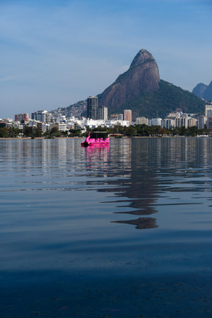 View of Rodrigo de Freitas Lagoon, south zone of Rio de Janeiro, Brazil. In the background, Dois IrmÃ£os hill and Pedra da GÃ¡vea. Sunny day. Buildings around. Pond water used for sports.の写真素材