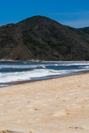Grumari beach near Barra da Tijuca in Rio de Janeiro, Brazil. Sunny day with blue sky, clear water and small waves. Hills and nature around.の写真素材