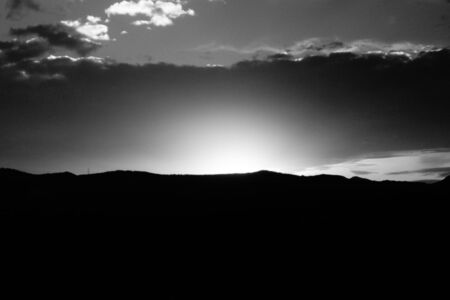 A sunset in black and white, with the sun hiding in the cloudy mountainsの写真素材