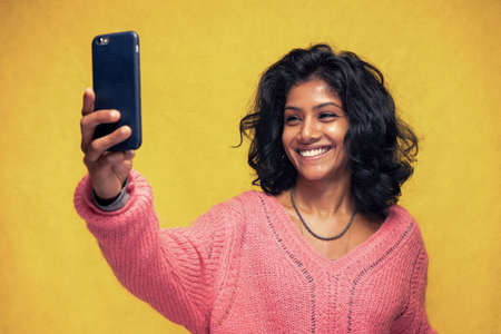 Beautiful Sri Lanka girl makes technology poses with yellow bright background - Young woman uses...