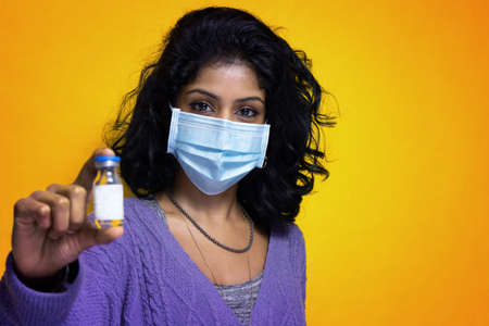 Pretty indian girl shows the  vaccine in her hands wearing  flue mask - Beautiful Sti Lanka young woman uses flue vaccine wearing  pandemic protectionの写真素材