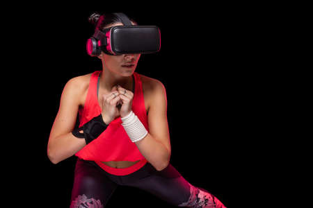 Beautiful sportive caucasian athlete sports woman training in pink undershirt with a black background - Studio shooting during gymnastics workout doing exercise wearing hi tech futuristic vr glassesの写真素材