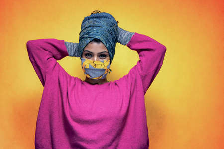 Beautiful young indian woman posing with  mask protection wearing a turban   posing with a yellow backgroundの写真素材