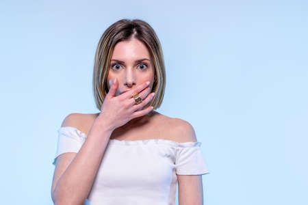 Young caucasian girl with light blue eyes covering her mouth surprised and astonished - Studio...