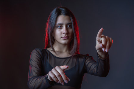 Portrait of beautiful cyber model woman posing wearing black leather leggings outfit with neon glow fluorescent led light in a black background typing in the airの写真素材