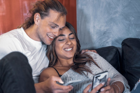 Cheerful couple of romantic caucasian guys smile sharing a night message in living room searching...