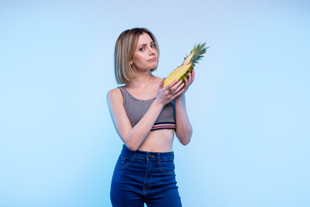 Young modern happy caucasian girl is forbidden with a light blue background - Studio photography of pretty model woman enjoy fruit looking at cameraの写真素材