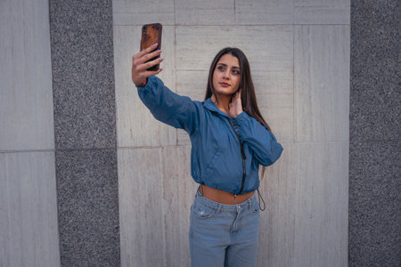 Stylish beautiful casual caucasian hip hop dancer chatting at smartphone in blue jacket, jeans,...