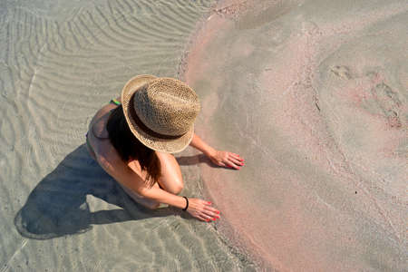 Beautiful woman wearing beach hat sitting on the nice pink sandの写真素材