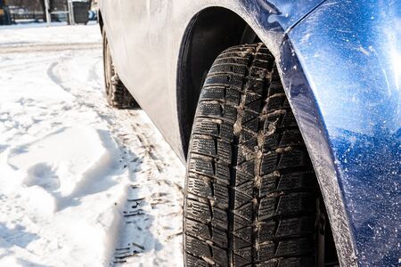 Close up of a car and winter tires. Very dirty car is parked on the street covered by snow.