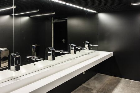 Modern public restroom with black walls and row of white sinks