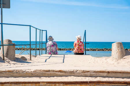 Two old women sitting on the stairs at the beach, and looking at the seaの写真素材