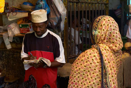 STONE TOWN, ZANZIBAR, TANZANIA - JULY 06 2008: Vendor Taking a Note. A transaction between a man and a woman at a market in Stone Town, Zanzibar.のeditorial素材