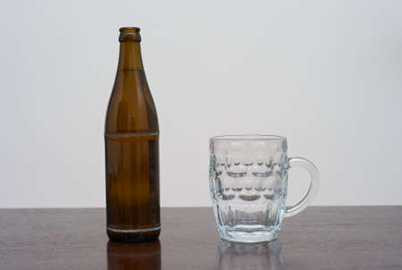 A Dimpled Pint Glass and a Bottle of Beer on a Brown Wooden Tableの写真素材