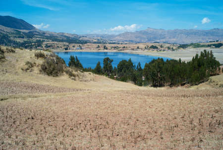 Mesmerizing Dark Blue Lake Surrounded by Dry Golden Grass Fields in the Peruvian Andes near Chinchero, Peruの写真素材