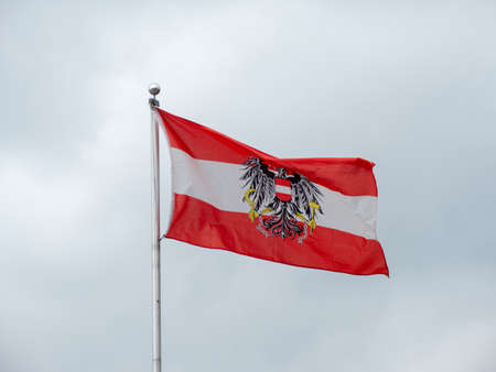Austrian Flag with the Federal Eagle Coat of Arms and Red, White and Red Colors flying on a Grey Backgroundの写真素材