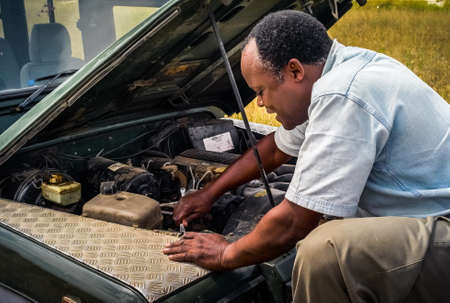 Serengeti, Tanzania - July 3 2008: Black man repairing a Landrover Safari Jeep in Africa. An african driver fixing a 4x4 vehicle after a breakdown.のeditorial素材