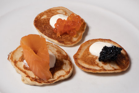 Mixed Blinis with Smoked Salmon, Rad and White Caviar garnished with Sour Cream on a White Plateの写真素材