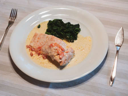 Salmon in Cream Sauce with Buttered Spinach on a White Plate with Silver Fish Knife and Forkの写真素材