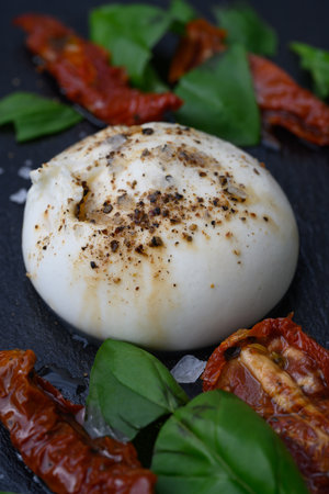 Burrata, an Italian Cow Milk Cheese made from Mozzarella, Stracciatella and Cream from Puglia, Italy, served with Salt, Pepper, Sun dried Tomatoes and Basilの写真素材