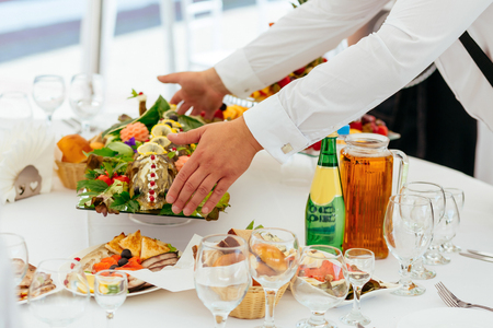 The waiter puts a big dish of fish with vegetables on the tableの写真素材