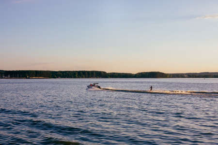 Water skiing on lake at sunset. Wakeboarder and boatの写真素材