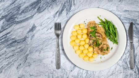 Pork tenderloin with potatoes and wild mushroom sauce and green beans on white plate laying on kitchen countertop. Top view with negative space.の写真素材