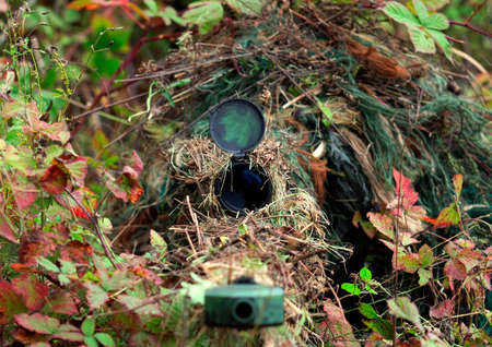 Camouflage Hunter or soldier hiding in bushes in camouflage autumn  background. Sniper with rifle.の写真素材