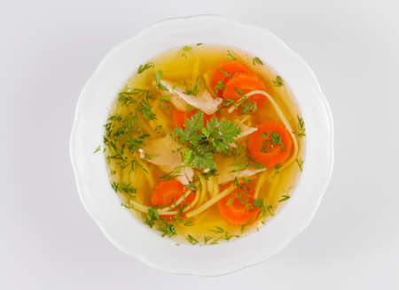 Chicken soup or broth with noodels, chicken meat pieces , carrot slices and herbs in white bowl.の写真素材