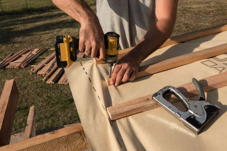 Roof construction building. Man using electrical scredriver to attach construction elements.の写真素材