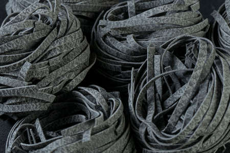 Raw uncooked black squid ink fettuccine pasta background.