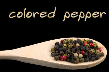 colored pepper on wooden spoon isolated on black background