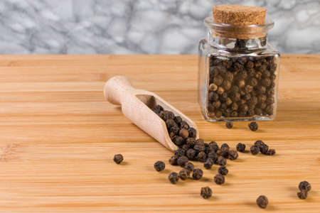 Black pepper peppercorns in wooden scoop and jar on bamboo desk. Closeup.