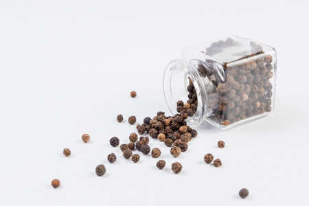 Black pepper peppercorns  in a glass jar isolated on white background.