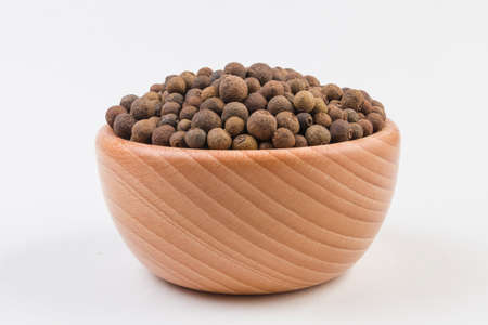Allspices or Jamaica pepper in wooden bowl isolated on white background. Closeup.