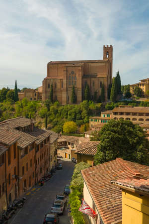 Scenic view of Siena cityscape over rooftops with San Domenico Basilica on background against blue...