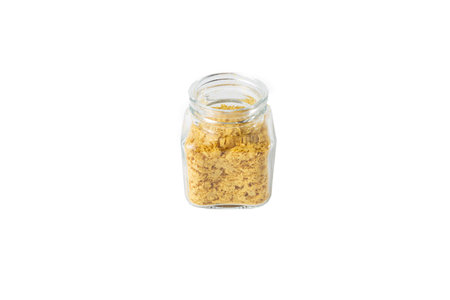 Savory vegan yeast flakes in a glass jar isolated on white background.