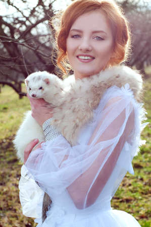 redheaded woman in white dress with a white ferretの写真素材