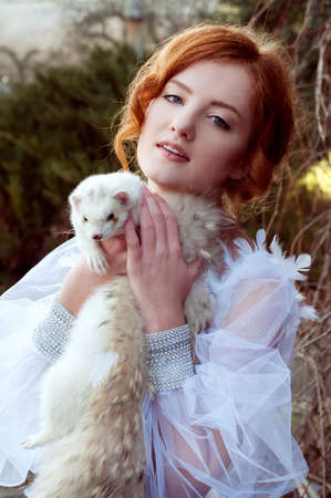 Redheaded princess with a white ferret in the woodsの写真素材