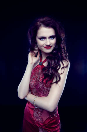 Beautiful redheaded woman with long curly hair in red evening dress smiling. Gypsy style.の写真素材