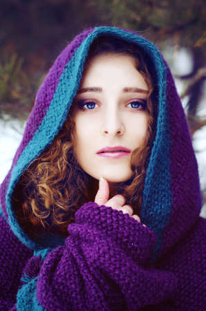 Mysterious young woman in purple knitted cape with a hood in winter forestの写真素材