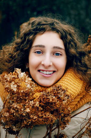 Attractive young woman with curly hair near dried hydrangea flowers wearing yellow snoodの写真素材